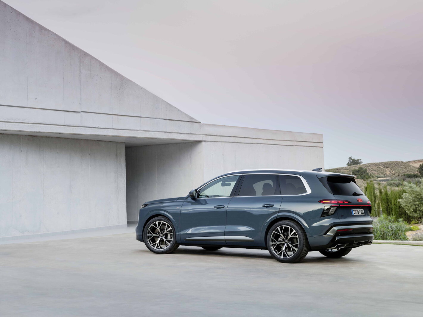Petrolblauwe Audi Q7 SUV, achterkant en zijkant, met strak design tegen moderne architectuur.