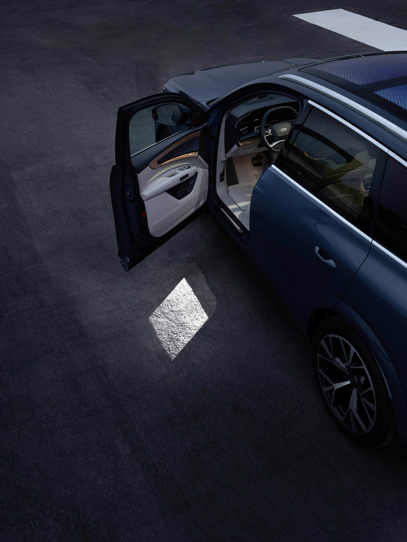 Audi Q7 met geopende deur, toont interieur en een lichtprojectie op de grond.