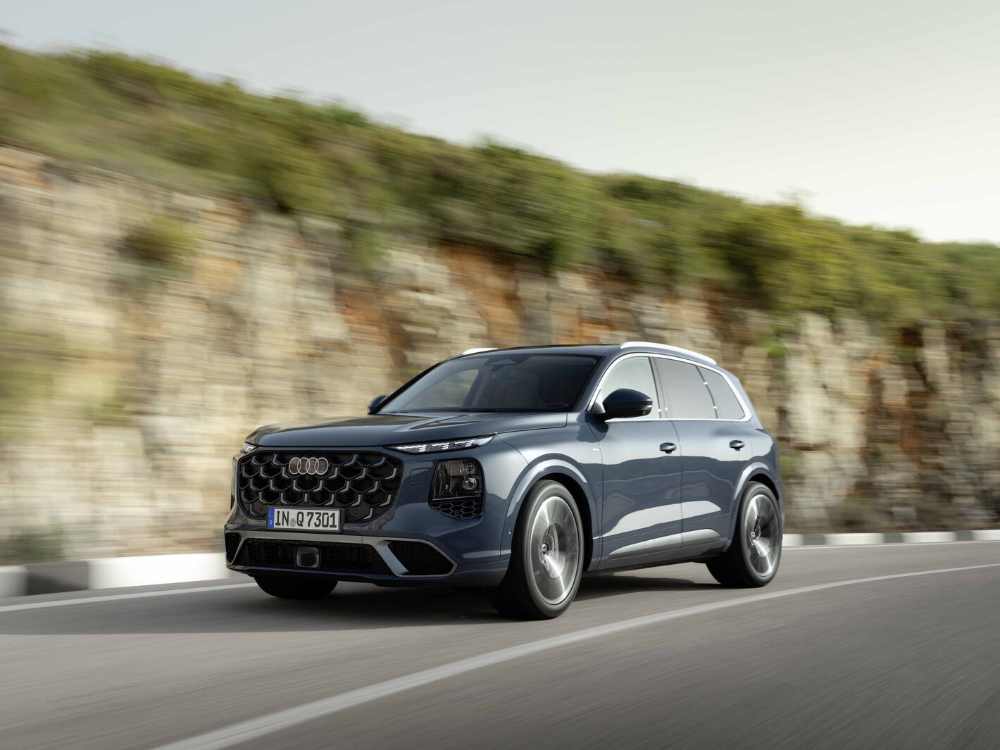 Donkerblauwe Audi Q7 SUV rijdt langs een kronkelende bergweg.