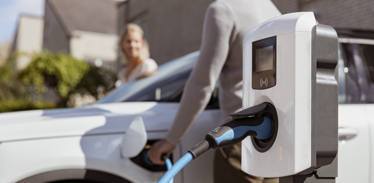 Koppel vertrekt met een witte elektrische auto en bestuurder trekt laadkabel uit